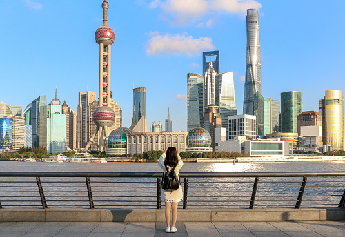 Female tourist on the Shanghai Bund taking a picture of the iconic Shanghai skyline view of Lujiazui. Shanghai a massive international city in China.