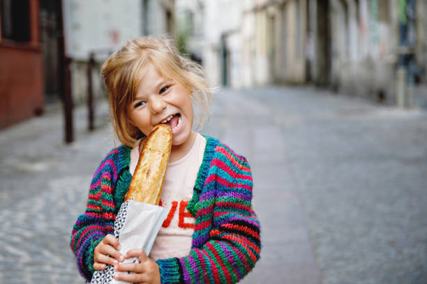 Adorable little preschool girl with fresh French baguette on the street side of the city. Happy small child in Paris, France. Adorable little preschool girl with fresh French baguette on the street side of the city. Happy small child in Paris, France bread bakery baguette french culture stock pictures, royalty-free photos & images