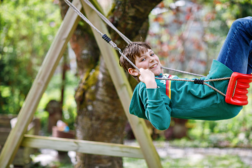 Happy school boy having fun on swing in domestic garden. Healthy child swinging under blooming trees on sunny spring day. Preteen Kid laughing and crying