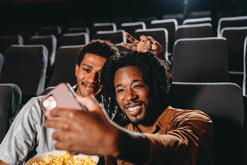 A couple is taking a selfie at the movie theatre. They are having fun together.