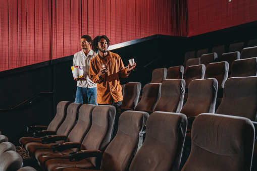 A gay couple is arriving at the movie theatre. They are looking for their chair.