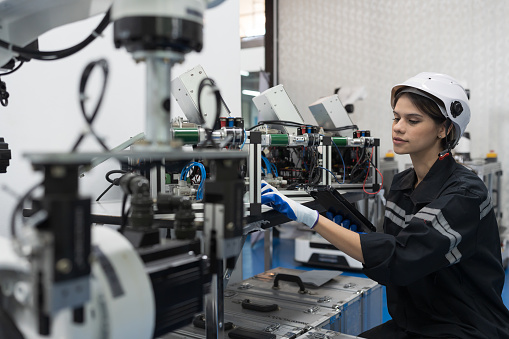 Female engineer control autonomous mobile robot or AMR in the manufacturing automation and robotics room. Female engineer inspecting quality of robotics arm