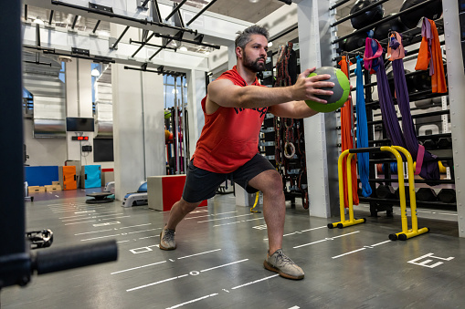 Handsome Caucasian bearded muscular man doing exercise with medicine ball in gym gym.