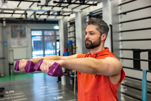 Adult bearded sporty man working on his biceps, lifting dumbbells arms workout in the gym.