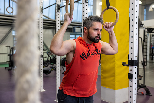 Adult bearded fit man pulling up on gymnastic rings in gym, training, training his biceps and triceps.