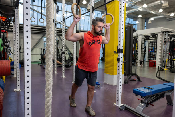 Powerful bearded man exercising with gymnastic rings at gym.