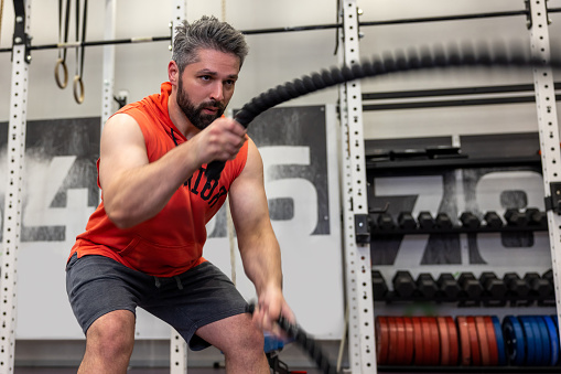 Strong powerful bearded man working out with battle ropes at gym, developing strenth and endurance.