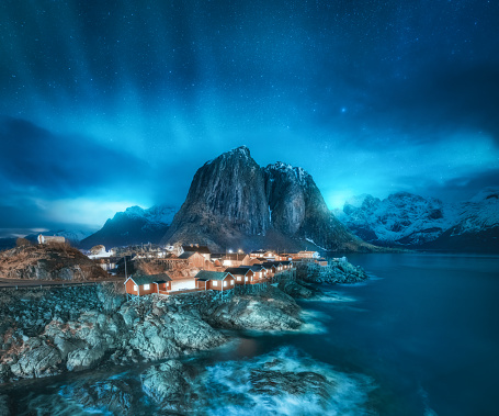 Auroras boreales en Hamnoy, Islas Lofoten, Noruega. Cielo estrellado y auroras boreales, montañas nevadas, costa del mar, rorbuer, rocas y piedras en el agua, luces de la ciudad en la noche de invierno. Luces polares brillantes photo