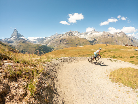 Woman on mountain bike riding on flow trail, Matterhorn mountain peak in distance, Switzerland.