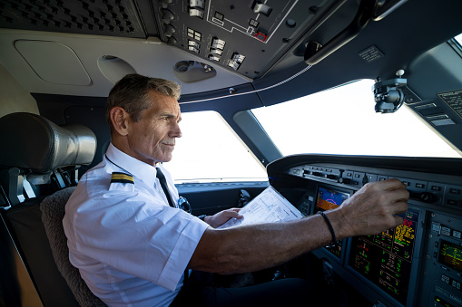 Portrait of a happy pilot in the airplane's cockpit looking at the camera smiling before take off - travel concepts