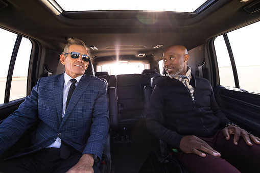 A mature White businessman sitting with his African American business partner inside a luxury SUV.