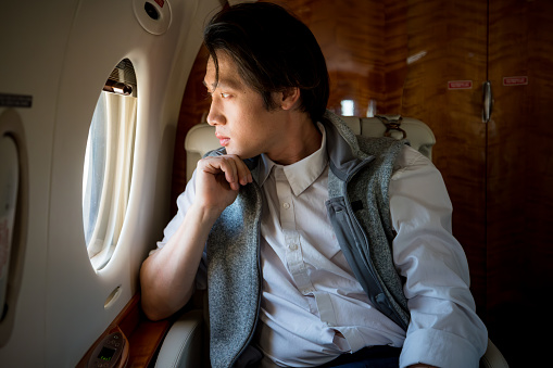 A young Asian man looking out a private jet's window.