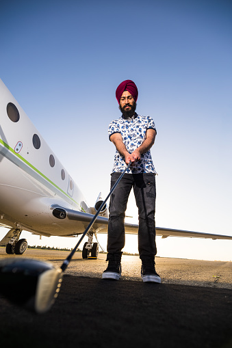 A young Indian man holding a golf club outside a private jet.