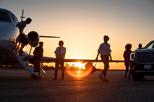 A group of passengers leaving private jet during sunset.