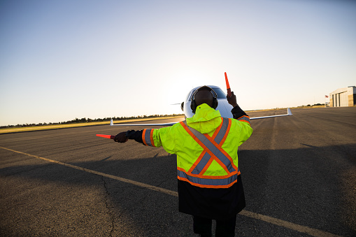 An African American marshal signals private jet on airplane runway.