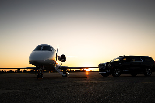 A black luxury parked in front of a private jet during sunset.