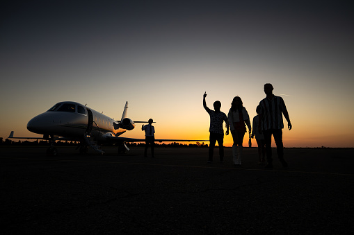 A picture of a group of people standing in front of a private jet at dusk.