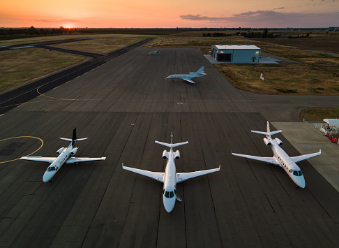 Four private jets parked on the runway, shot at sunset.\n\nThis drone shot was taken with full permission and co-operation of the airport staff and the pilots of the aircraft.
