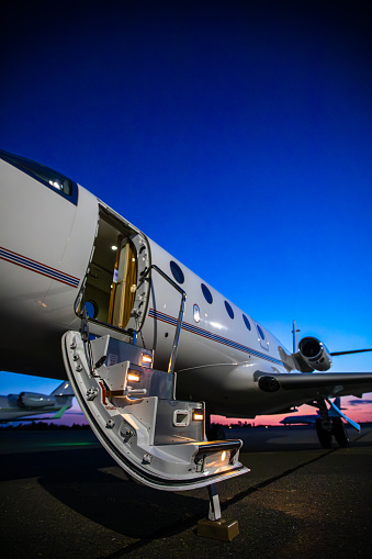 A vertical still image of an open door into a private jet,  taken at sunset.
