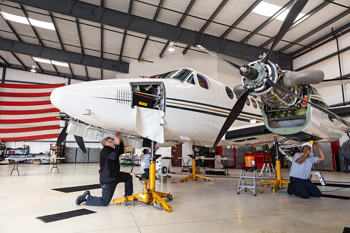 Mechanics repairing private jet inside the hangar of a small general aviation airport in California.