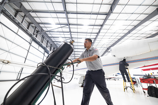 An airplane mechanic carrying a black cylinder inside the hangar of a small general aviation airport in California.