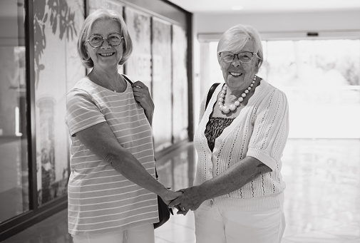 Black and white portrait of two white-haired senior women enjoying shopping at mall, elderly grandma couple looking for sale