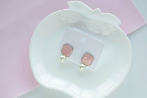 istock Rose quartz stud earrings in the shape of a square with pearls on a white cup. Romantic jewelry. The advertising concept of the product 