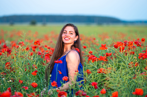 elegant young woman with long hair playing with petals in poppy field in evening sunlight