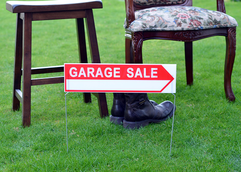 Closeup of a generic garage sale sign with arrow in front of some items for sale on a lawn.