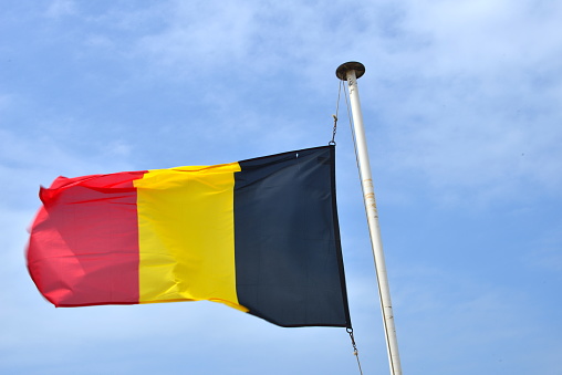 Belgian waving flag in portrait in front of a blue sunny sky
