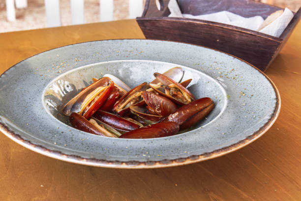 Cooked Lithofaga date shell mussels served on a dish at a wooden table. stock photo
