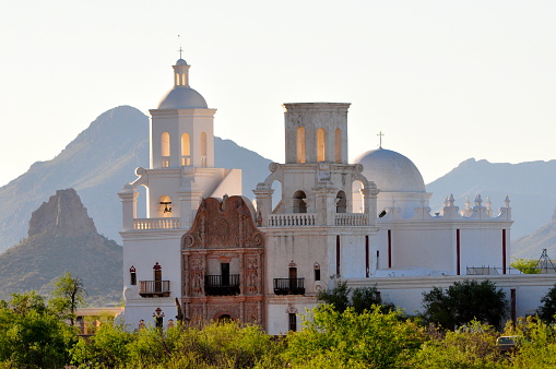 Mission San Xavier Del Bac provides the foreground for mountains.