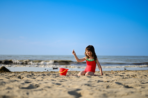 child holding a seashell while sitting on a sand.