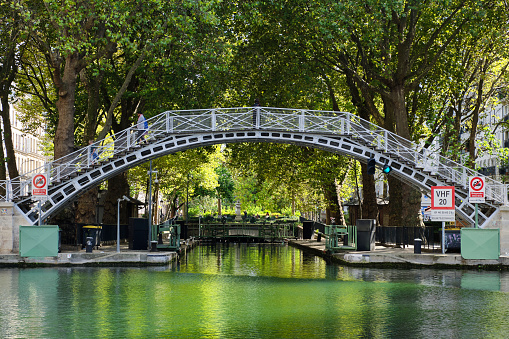 Paris, France -- September 18, 2022: Canal Saint-Martin, weaves its way through the heart of the Paris. Stretching an impressive 4.6 kilometers (2.86 miles), this picturesque waterway serves as a vital connection between the Canal de l'Ourcq and the majestic river Seine. Along its course there are 9 locks, one of which is pictured here. A significant portion, approximately 2,069 meters (2,263 yards) long, had been concealed beneath the surface during the mid-19th century. The aim was to create expansive boulevards and inviting public spaces above, leaving only traces of the covered canal visible.