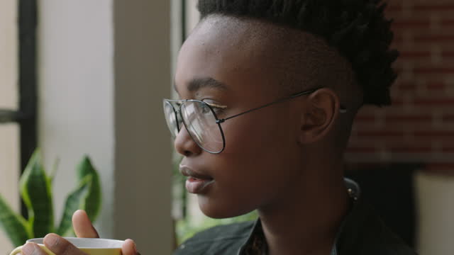 portrait stylish young african american woman student drinking coffee at home looking out window thinking planning ahead enjoying relaxing lifestyle wearing trendy fashion glasses