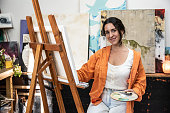 Portrait of a mid adult woman painting on a canvas while hold a artist's pallet at home