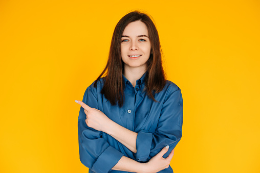 Engaging Businesswoman: Confident Young Female in Formal Office Attire with Bright Smile, Pointing at Blank Space - Isolated on Vibrant Yellow Background.
