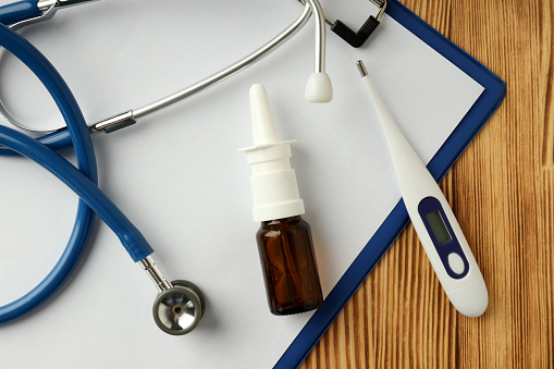 Nasal spray, stethoscope, thermometer and clipboard on wooden background