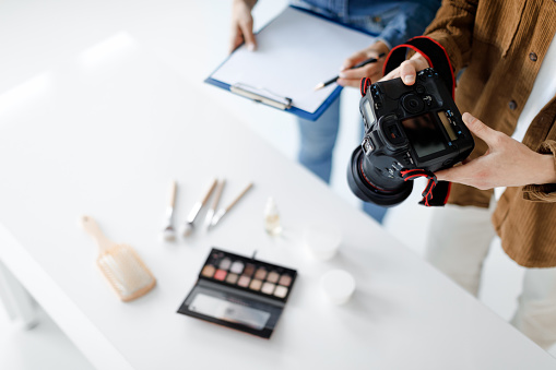 Object photography concept. Male photographer taking photo of cosmetic products on desktop, working in team with assistant, man holding camera, making content photoshoot