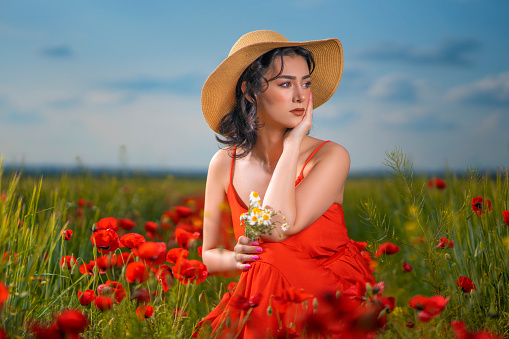 Young beauty walking in poppy field. traveler young woman in red dress and hat