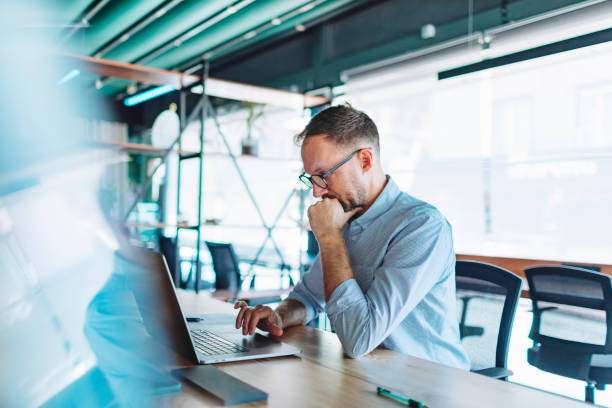 istock Young adult man working in coworking using laptop 1495205285