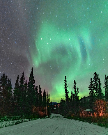 Bright aurora borealis seen in northern Canada along the Alaska Highway with snow covered road and starry sky background, wallpaper, desktop.