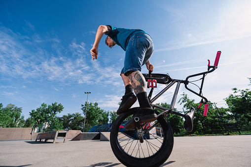 An urban middle-aged man is performing a 360 rotation on one wheel on his bmx in a skate park. A tattooed mature professional bike rider is balancing on on wheel of his bike.
