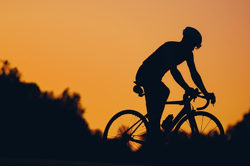 Silhouette of an athletic man in sport clothes riding a bicycle outdoors during a sunset. Concept of people, healthy lifestyle and recreation. Sport cycling. Copy space. Sunset.