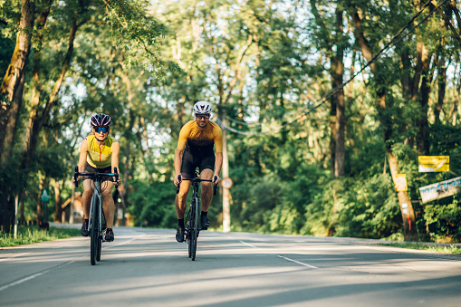 Front view shot of a couple wearing sportswear and protective helmet while riding bike outside of the city. Competition and regular training. Concept of people, workout and favorite hobby.