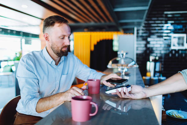 istock Young adult man paying for coffee at cafe using smartphone 1495207693