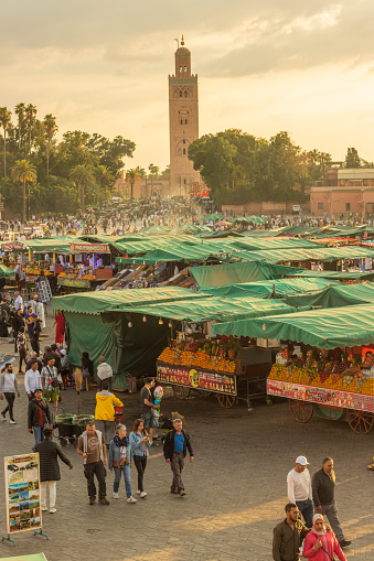 Many market stalls and people walking around Djemma el Fna Square in Marrakesh, Morocco, at dusk.
