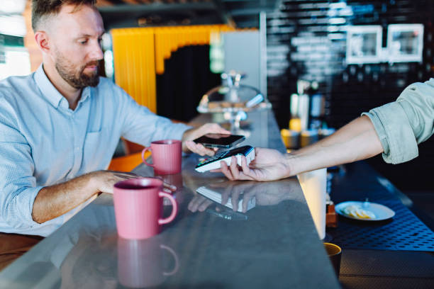 istock Young adult man paying for coffee at cafe using smartphone 1495208027