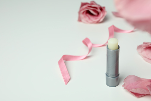 Hygienic lipstick and roses on white background