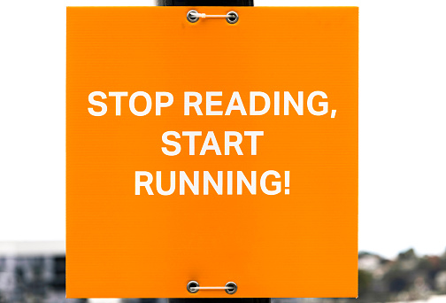 Outdoor orange sign STOP READING, START RUNNING, background with copy space, full frame horizontal composition